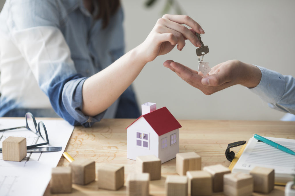 Man collecting keys for a new house from woman with a small model of a house on the table