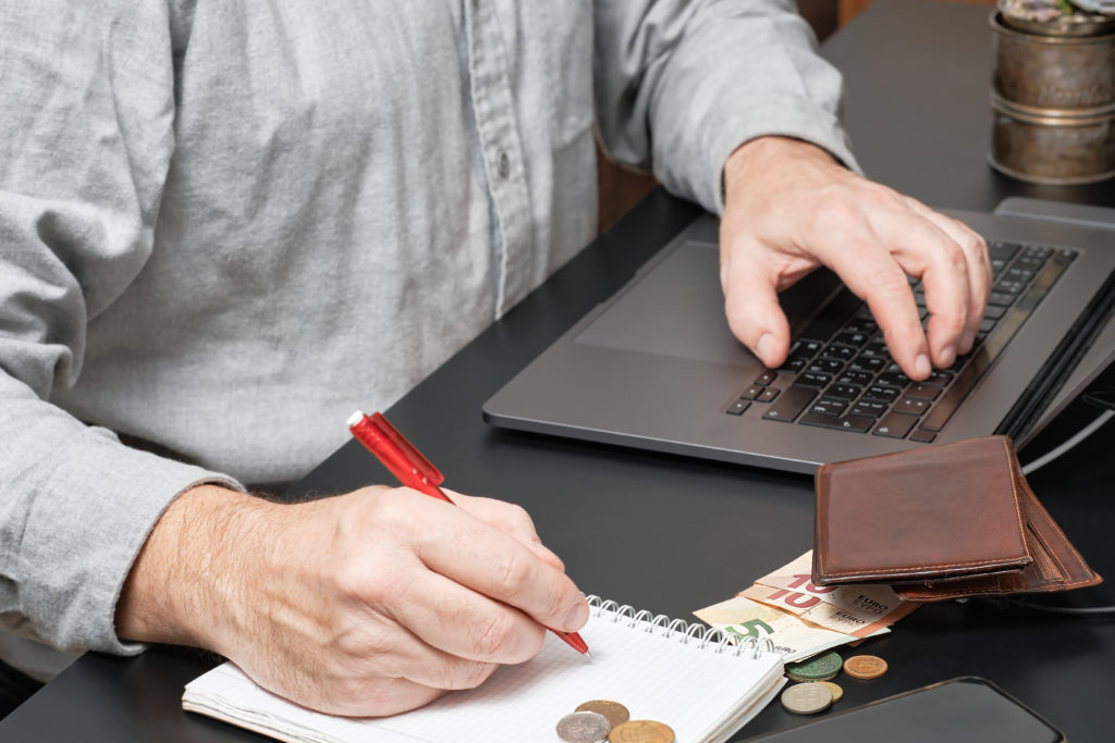 Man writing down his debts, using laptop to look at finances