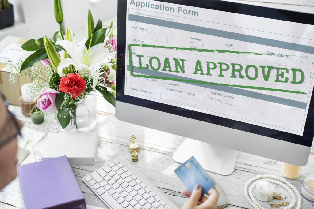 Loan approved on a computer monitor, with woman holding a credit card up