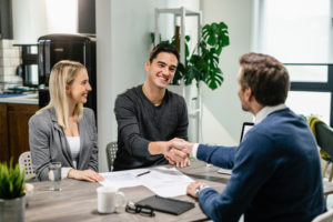 young happy couple making agreement with their financial advisor home men are shaking hands