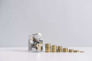 glass jar full money front decreasing stacked coins against white background